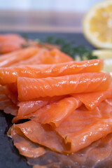 Slices of tasty smoked Scottish salmon fish served on black plate with lemon and fresh dill