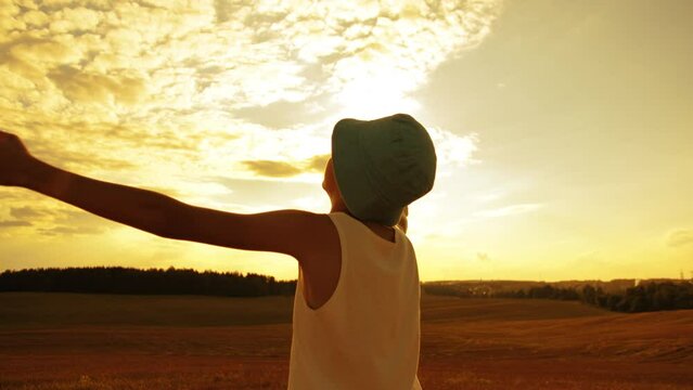 boy raises his hands to the sky on mars, boy in a hat raises hands to the sky in the field sun glare at sunset
