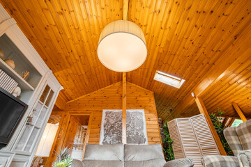 Bright living room with furniture, big lamp and sloping ceiling in a wooden cottage.
