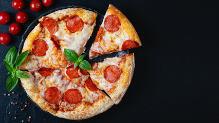 Hot pepperoni pizza and cooking ingredients tomatoes basil on black concrete background. Top view of hot pepperoni pizza. With copy space for text