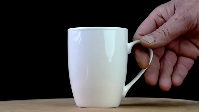 Human hand put empty or full white coffee or tea cup on wood table on black background.