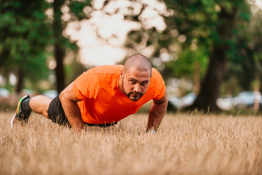 Young man working out doing push-ups in park as he warms up for his daily workout or jog