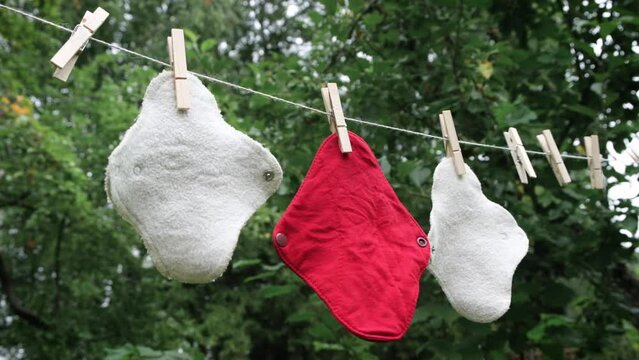 Three reusable cloth sanitary menstrual pads hanging to dry on clothesline in the garden. Zero waste period. Feminine washable, eco friendly personal hygiene supplies. Womens health care. Sustainable.
