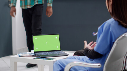 People sitting in waiting area with greenscreen template on laptop, looking at isolated chroma key background. Blank mockup display with copy space template in hospital reception.