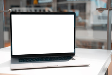 Laptop with white screen in business office or shopping mall. Empty copy space, blank screen mockup. Soft focus laptop with interor background. Travel, study and office work concept