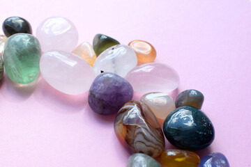 Semi-precious beautiful stones of bright colors lie on a pink background. Amethyst, rose quartz, agate, apatite, aventurine, rock crystal on a pink background. Selective focus.