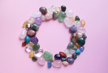 The circle is lined with natural minerals. Semi-precious stones of different colors, raw and processed. Amethyst, rose quartz, agate, apatite, aventurine on a pink background.