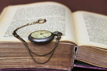 Eine antike Taschenuhr lehnt an einem alten Buch mit vergilbten Seiten - obrazy, fototapety, plakaty