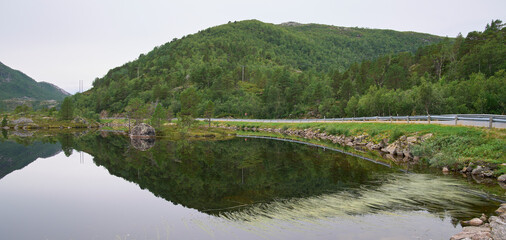 Fototapeta na wymiar Morning landscape with symmetry reflection in the water of a lake. Mirror surface of a lake. Mountain range and forest at the background. Silence and calm. Remote part of Lofoten, Nordland, Norway.