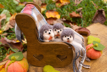 Three small felted hedgehogs on a wooden chair with a plaid on a wooden background with autumn decor