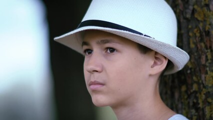 boy angrily looks at people passing by in the park, portrait of a boy sitting under a tree in the park