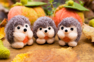 Three small felted hedgehogs on a wooden background with autumn decor