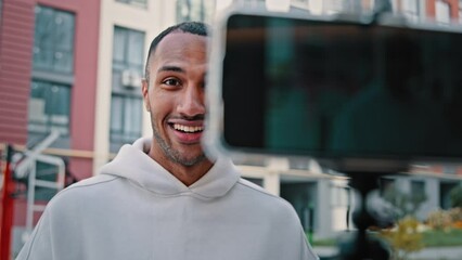 African biracial latin sportsman trainer handsome blogger put mobile phone on tripod record video vlog from sports ground training online promoting fitness exercises tutorial blog of healthy lifestyle