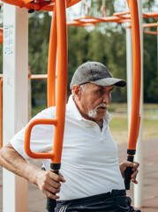 Obraz premium Persistent mature man with disabilities doing fitness exercises on outdoor simulator, pumping muscles and training endurance, rehabilitation, work on oneself, the desire to be healthy