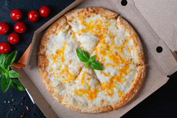 Pizza in a cardboard box on a black chalkboard background. View from above. Pizza delivery. Pizza menu