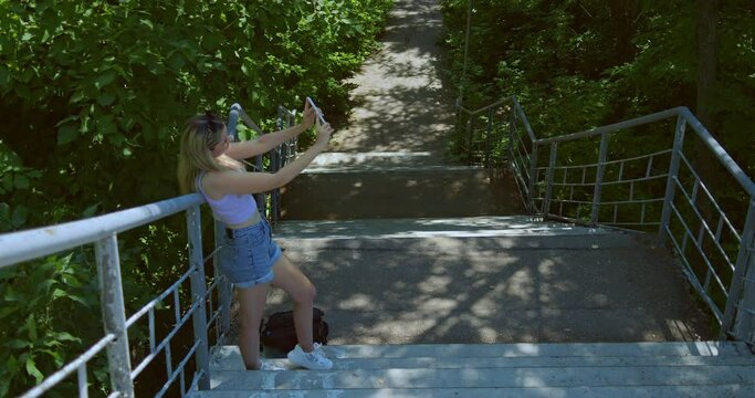 Pretty woman takes a selfie on a smartphone in the park on the stairs, modern youth with selfie addiction, a young woman takes a picture of herself on the camera of a modern mobile phone, a general