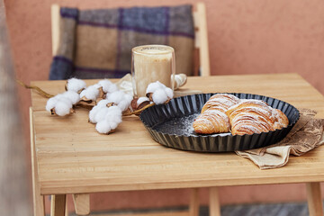 Aesthetic french breakfast outside - fresh croissants, cup of coffee, plaid at the terrace. Autumn coziness. Cotton decoration. Pastel background