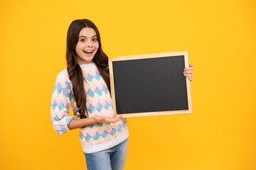 Naklejka na ściany i meble Teenage girl child holding blackboard, isolated on a yellow background.
