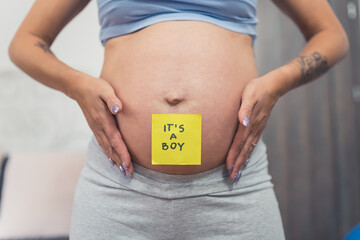It's a boy. Close up baby bump of a pregnant woman with a sticker on it. Surprise gender reveal...