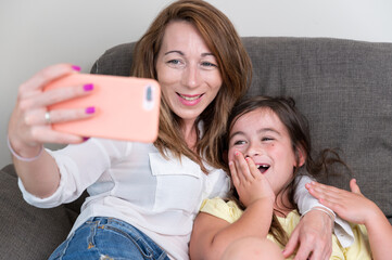Happy mother with her daughter are making a video call to father or relatives in a sofa. Concept of technology, new generation, family, connection, parenthood. High quality photography