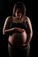 Young Brunette woman looking down at her big baby bump, studio light used.