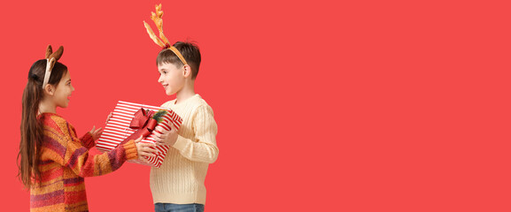 Fototapeta premium Funny little children with reindeer horns and Christmas gift on red background with space for text