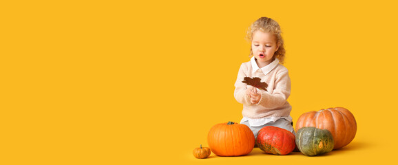 Cute little girl in warm sweater, with autumn leaf and pumpkins on yellow background with space for text