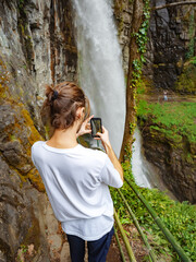 A young man photographs a huge waterfall. Huge waterfall in a green rocky gorge. Journey to the mountain waterfall.
