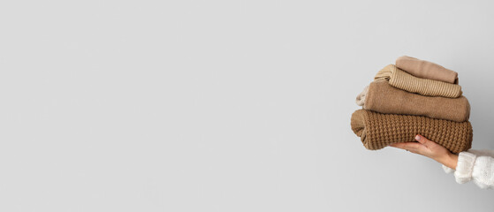 Hands of woman with stack of warm sweaters on light background with space for text