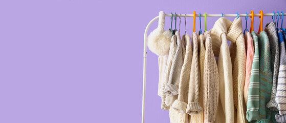Rack with children sweaters near lilac wall in room