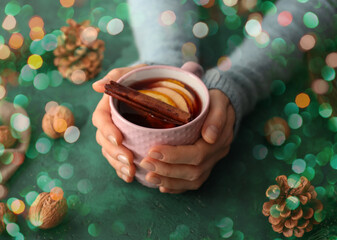 Female hands holding cup of delicious mulled wine on green background, closeup