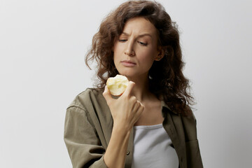 Confused pensive curly beautiful woman in casual khaki green shirt eat apple looks at it with...