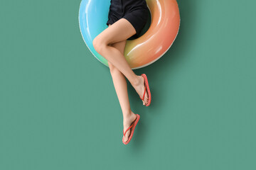 Beautiful young woman with inflatable ring on green background, top view