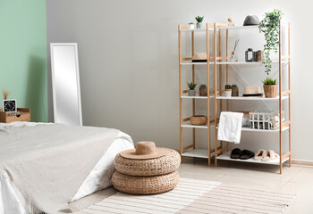 Interior of cozy bedroom with rattan poufs, mirror and shelving unit