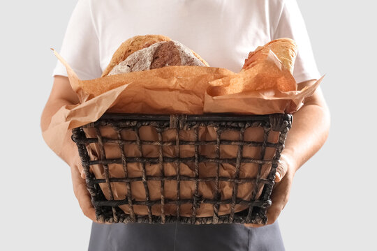 Man holding basket with loaves of fresh bread and parchment paper on light background
