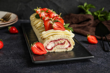 Fototapeta na wymiar Board with tasty strawberry roll cake on dark background