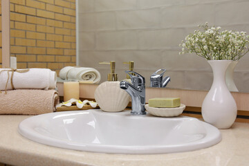 Bath accessories with sink, flowers and candle on table in bathroom