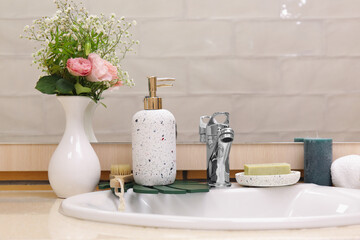 Bath accessories, sink and vase with flowers on table in bathroom