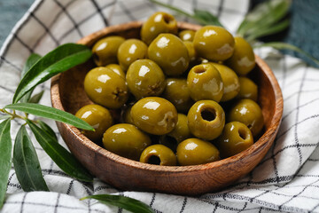 Bowl of delicious green olives on fabric background, closeup