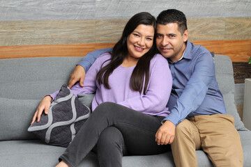 Latino man and woman couple sitting in an sofa in the living room enjoying their company and...