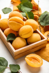 Wooden box of ripe apricots with green leaves on light background, closeup