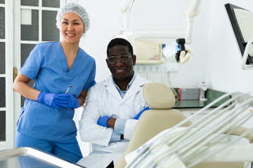 Portrait of smiling african-american man dentist and asian woman assistant in office of dental clinic.