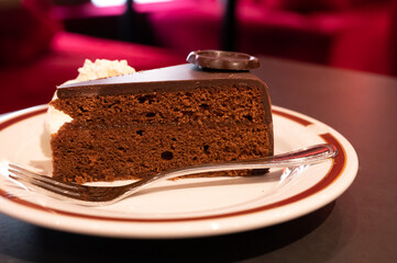 Piece of famous Sachertorte chocolate cake with apricot jam of Austrian origin served with whipped cream