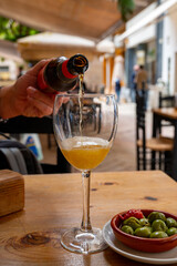 Pouring of beer from bottle in Spanish outdoor cafe, tapas bowl with green olives
