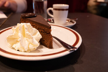 Piece of famous Sachertorte chocolate cake with apricot jam of Austrian origin served with whipped cream