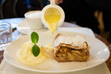 Austrian sweet dessert, portion of apple strudel with whippen cream and hot vanilla sauce served in old bakery cafe in Vienna, Austria