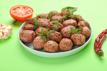 Plate with tasty meat balls and vegetables on green background