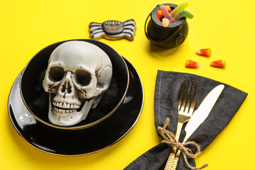 Table setting with scull and Halloween decor on yellow background, closeup