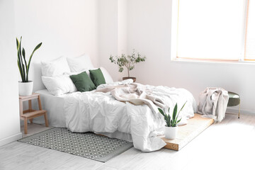 Interior of light room with big bed and houseplants