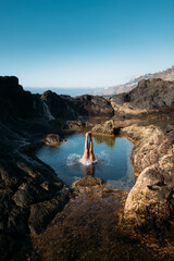Piernas de una chica joven saltando al agua en una piscina natural